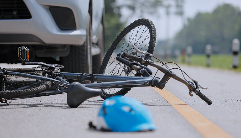 bicicleta en la carretera con un casco, detras se ve un coche. Ha habido un accidente con un ciclista y no saben si hace falta atestado o no